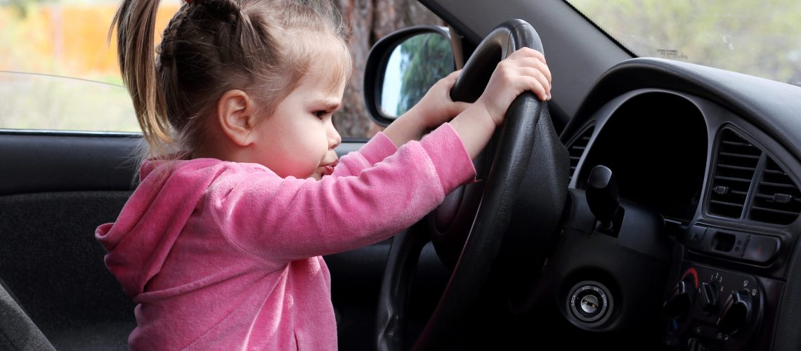 Little girl sitting behind the wheel of a car with a busy face, outdoors, family travel concept
